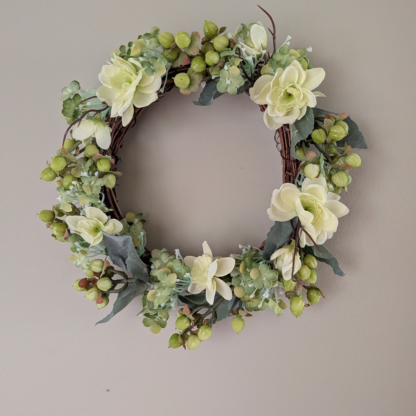 Floral  20cm wreath base with delicate soft green faux flowers and berries on a plain background