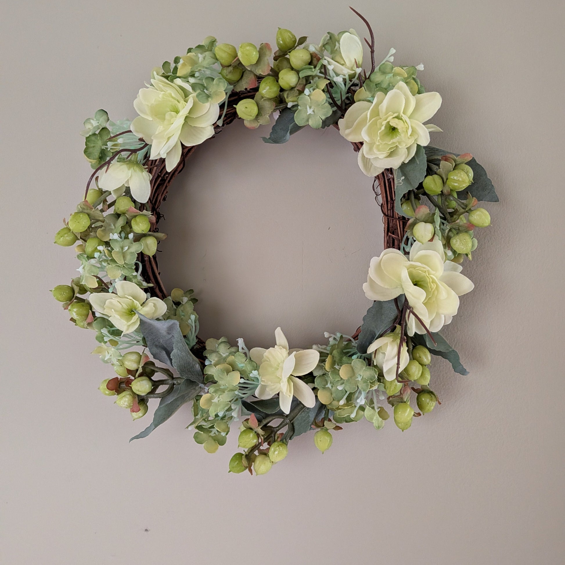 Floral  20cm wreath base with delicate soft green faux flowers and berries on a plain background