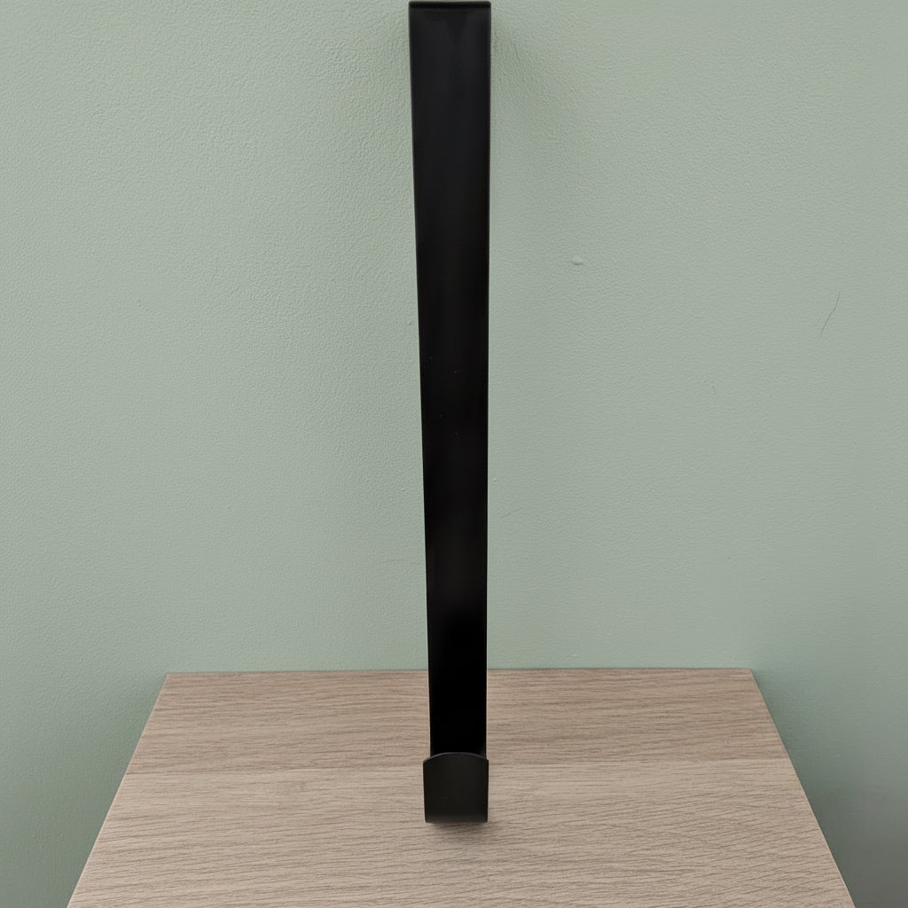 Black metal wreath hanger 30cm standing upright on light oak surface against sage green background
